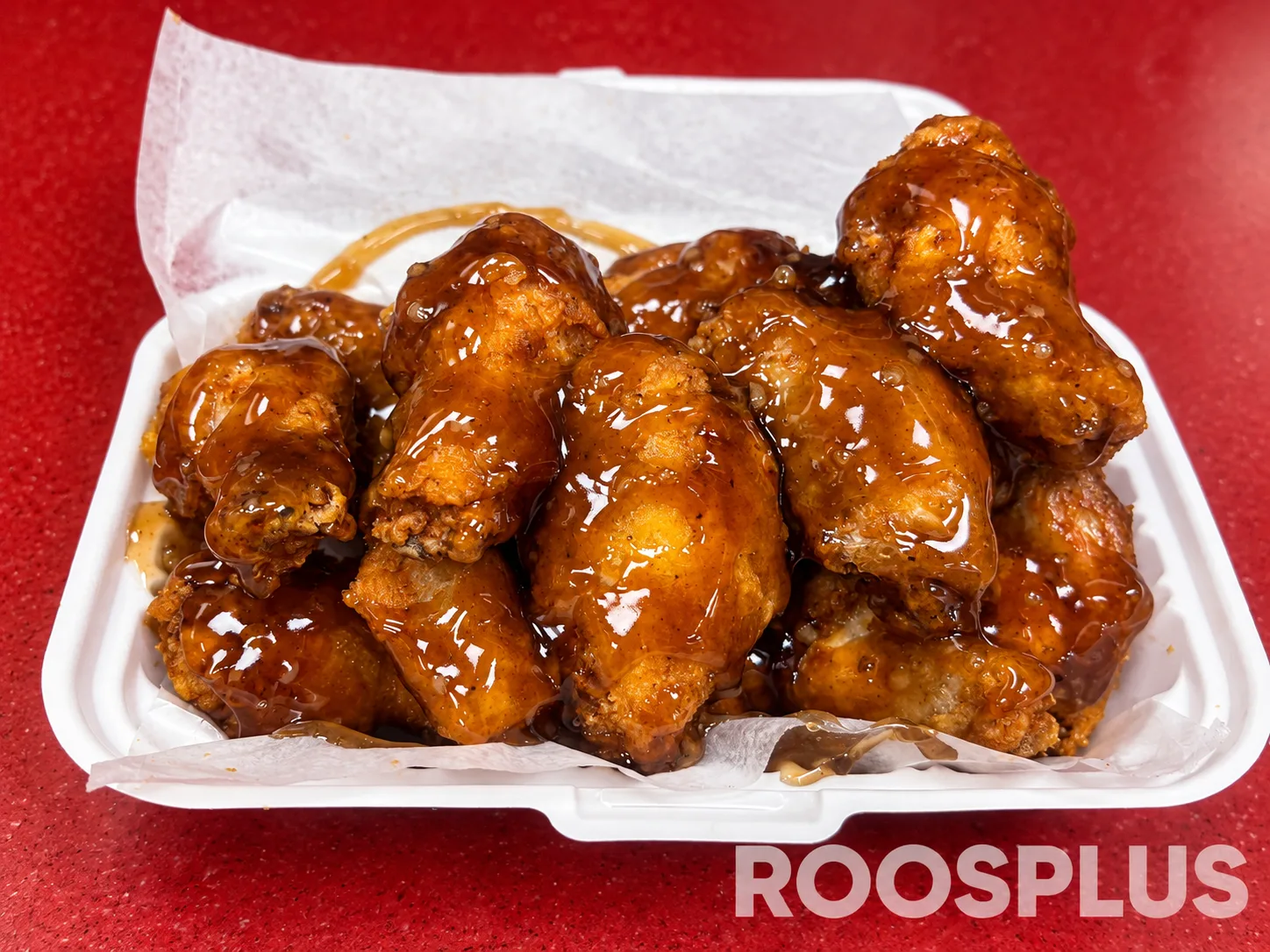 Chicken wings covered with a glossy brown glaze in a paper-lined takeaway tray at Bismillah Pizza, Eglinton Avenue East, Scarborough.