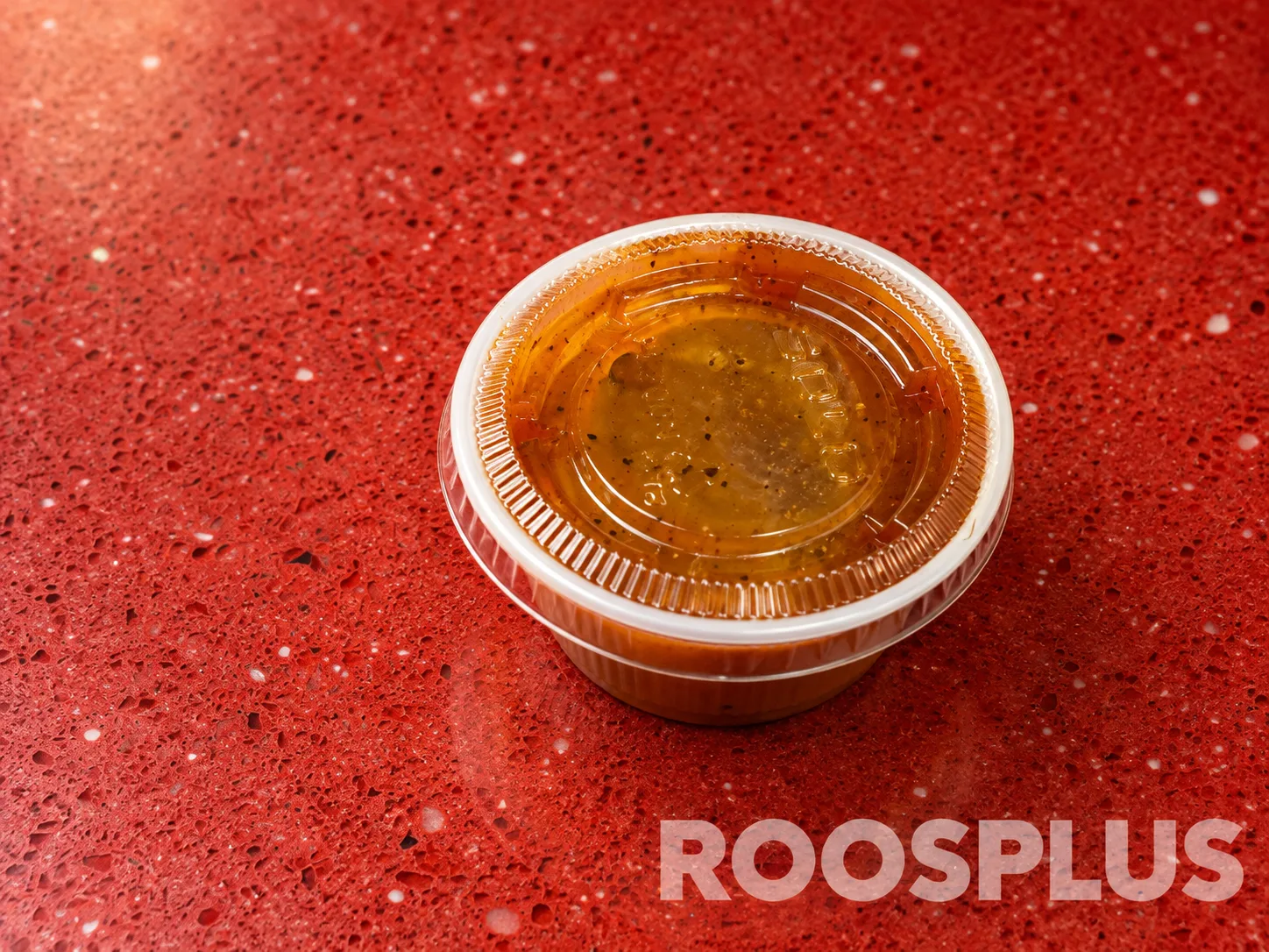 A sealed clear cup of golden dipping sauce with visible seasoning at Bismillah Pizza, Eglinton Avenue East, Scarborough.